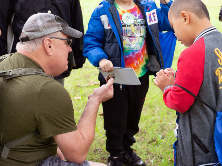 students gathered around a kneeling teacher examining a plant